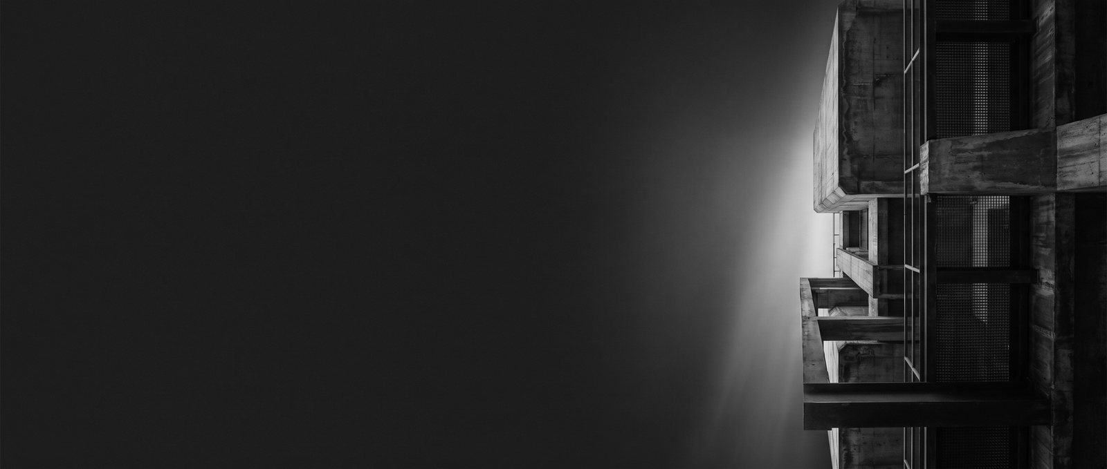 Conceptual editorial illustration — an almost invisible architectural structure emerging from deep graphite darkness under a single plane of white light. Monochrome study; not a photograph of a real facility.